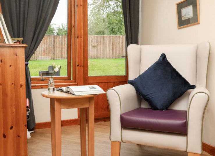 cosy reading area within care home bedroom. A chair sits next to a table with an open book