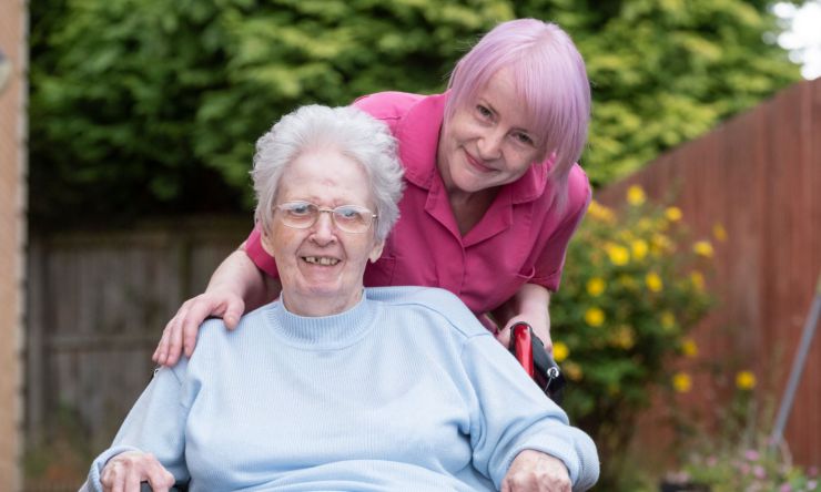 a staff member assisting a resident, pushing her in a wheelchair and smiling