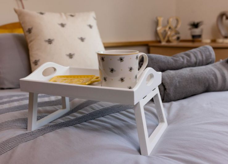 A white breakfast tray with a mug sitting on top of grey bedsheets close zoom, cosy atmosphere