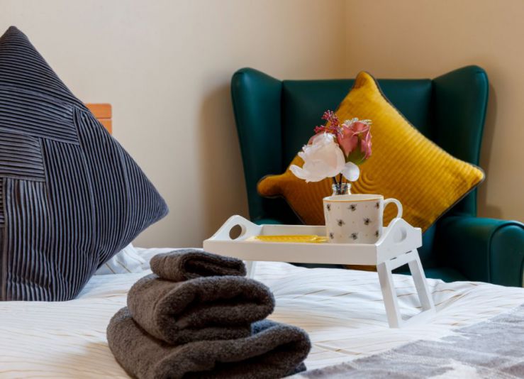 bedroom set up - towels and breakfast tray sitting on bed, with a chair with a yellow cushion in the background