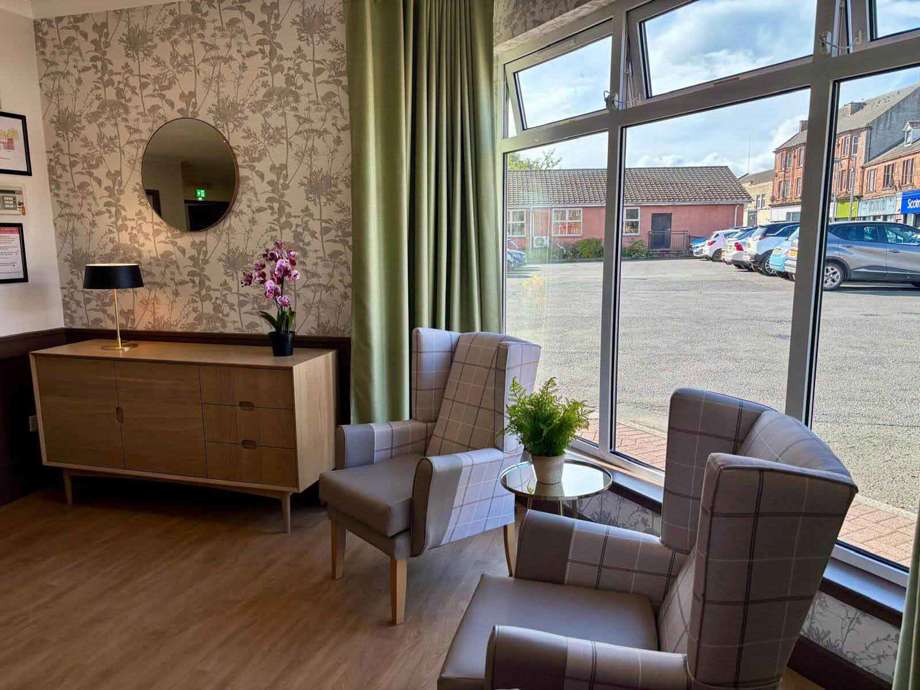 A modern lounge room with neutral colours, wingbacked chairs, and large windows looking out to the homes car parking area