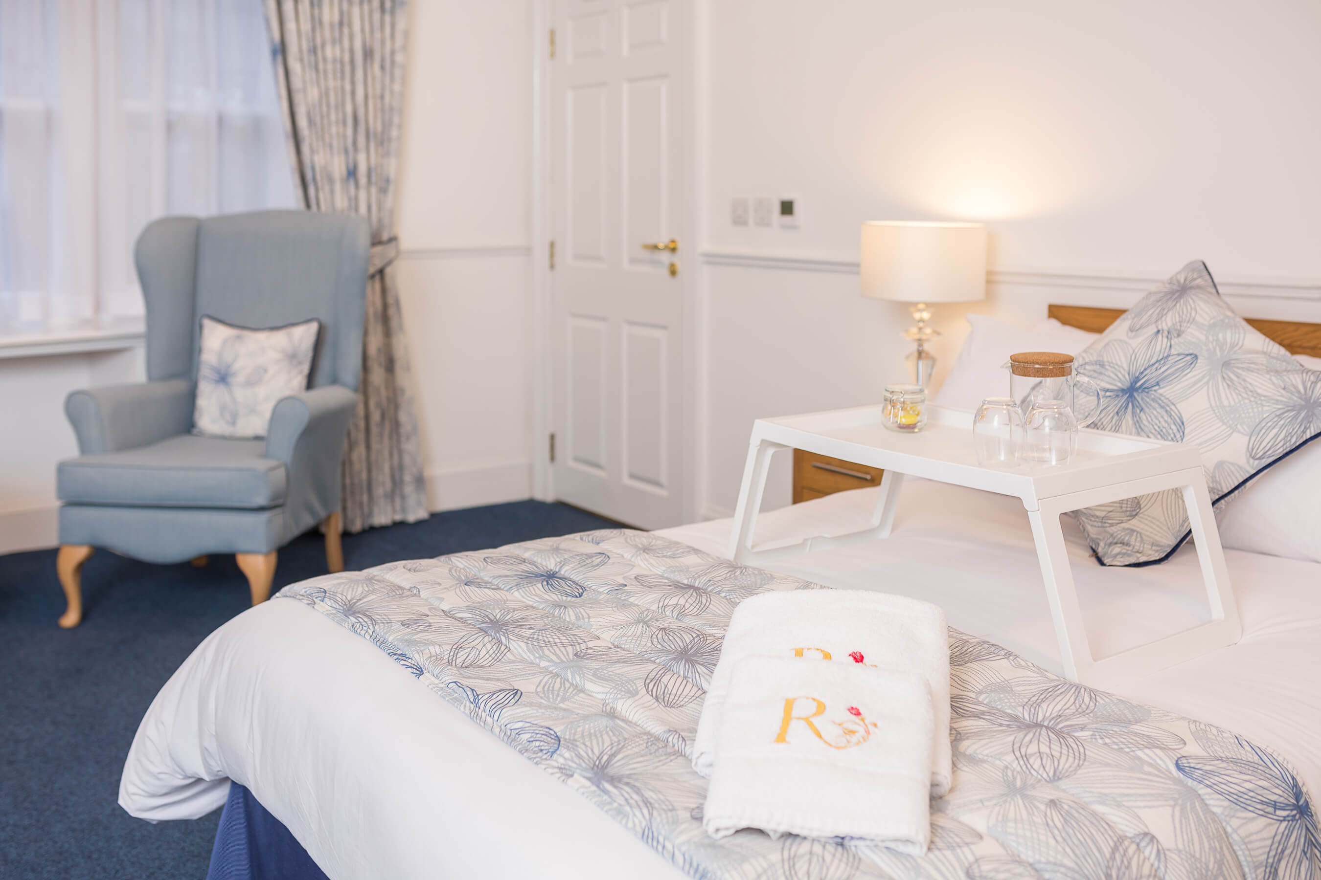 Homey bedroom features clean white walls, neutral furniture with pops of cosy blue, and plush Renaissance At towels