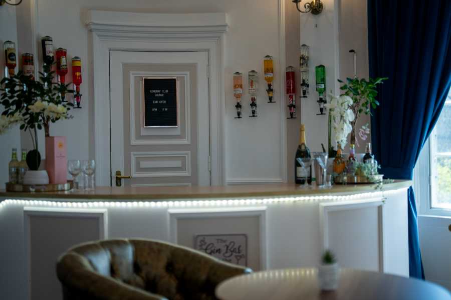 Elegant white bar showcasing a variety of liquors and glassware. Bottles adorn the wall, complemented by decorative glasses and flowers