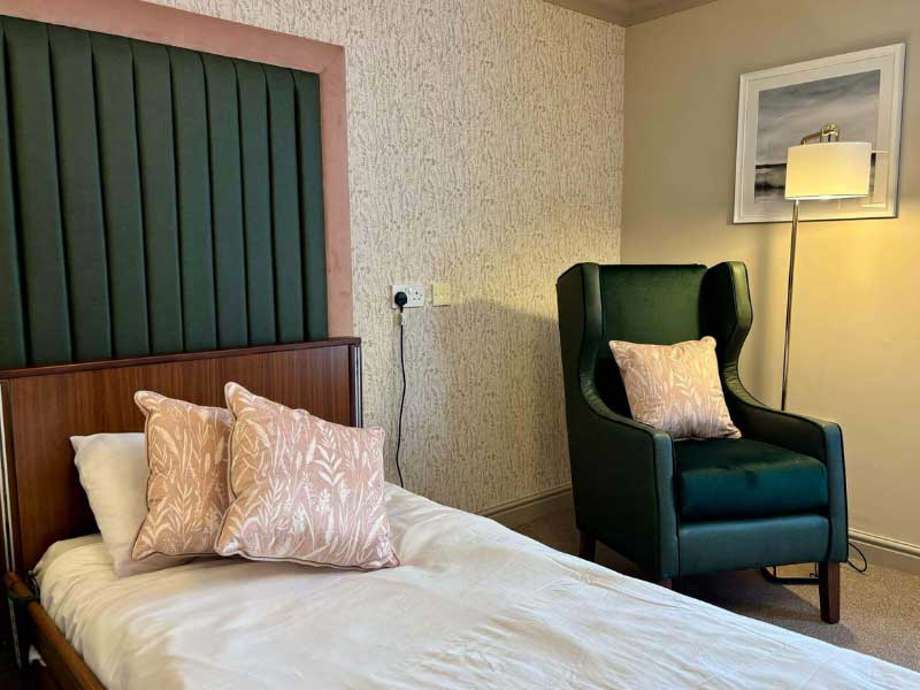 Modern bedroom with a prominent green and pink color scheme, bed with floral cushions, green chair, and floor lamp