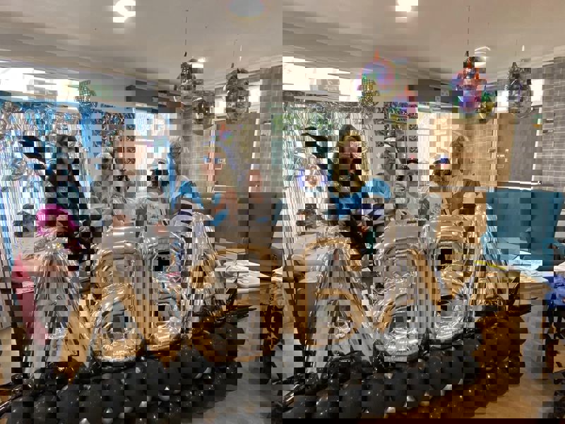A group of care home residents and staff celebrating 50 years of ABBA with large balloons and themed decor