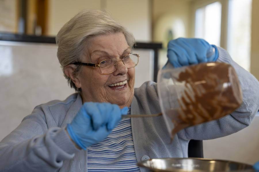 A care home resident smiles as she pours melted chocolate into a large bowl for baking