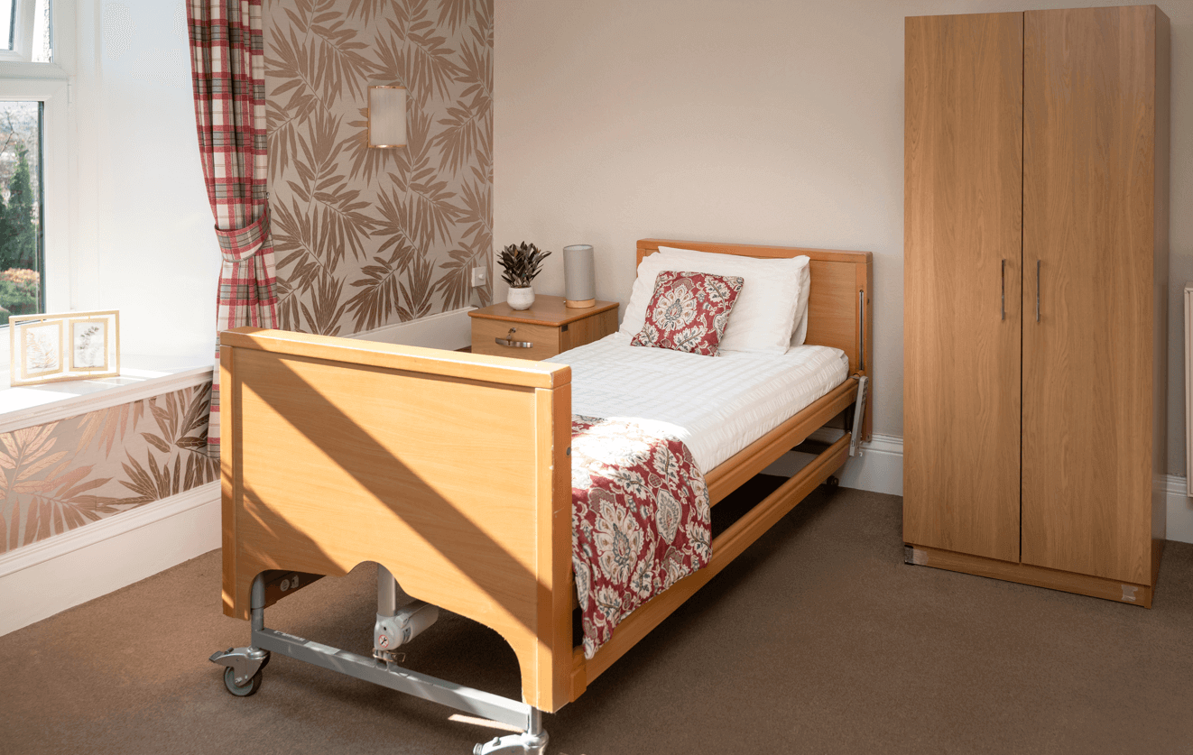A warmly decorated room in shades of copper and red, furnished with a bed, a wardrobe, and a bedside table. Lots of natural light floods this room.