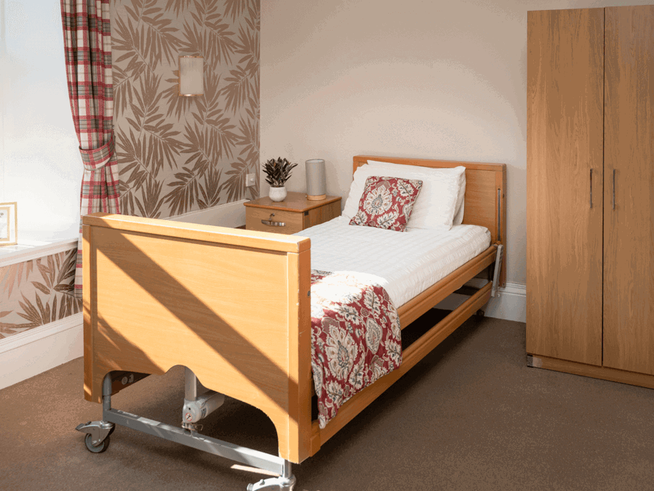 A warmly decorated room in shades of copper and red, furnished with a bed, a wardrobe, and a bedside table. Lots of natural light floods this room.