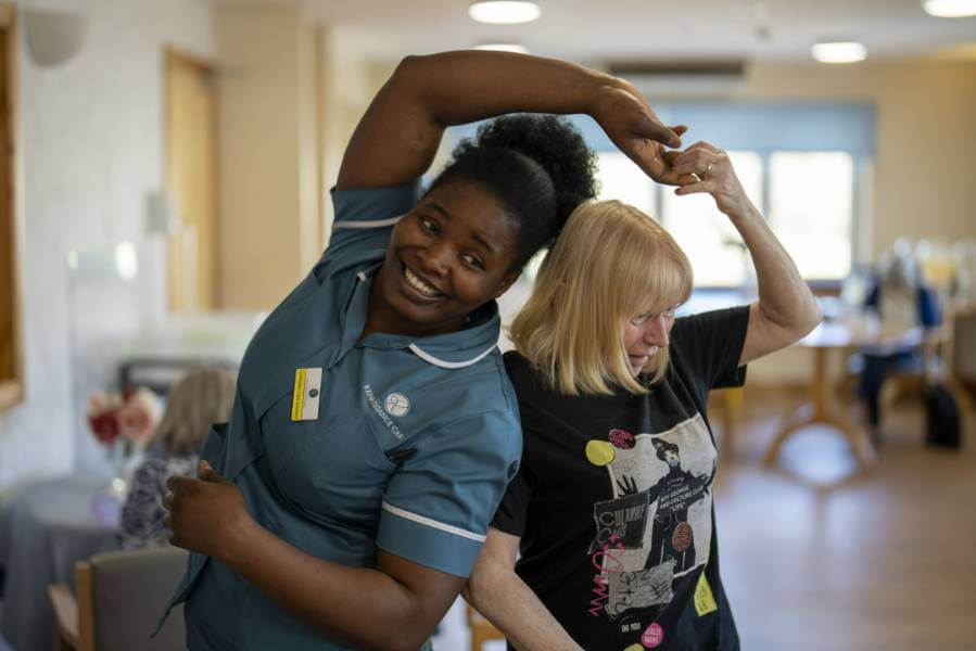 Staff member and resident dance together in a communal lounge