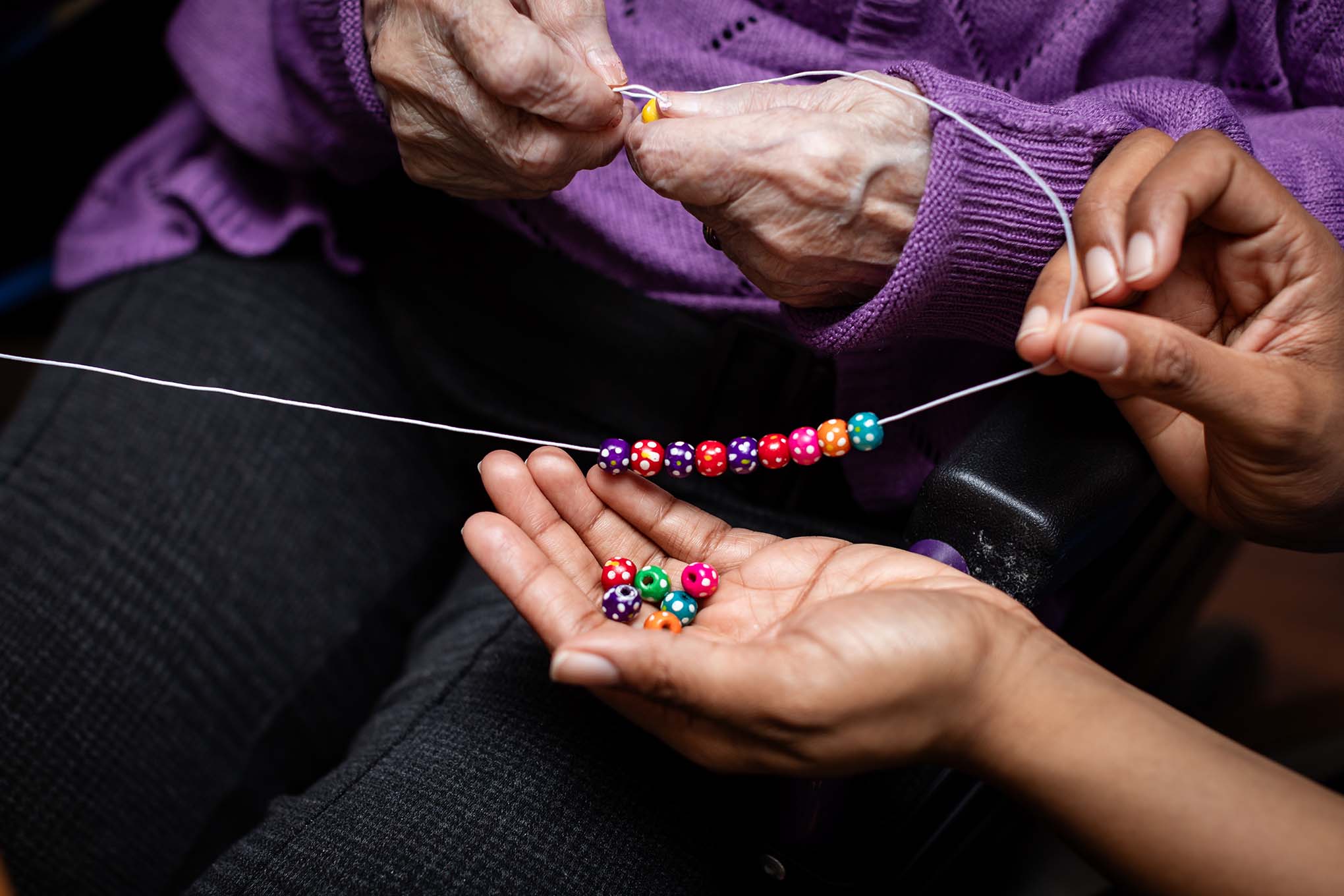 A staff member supports a resident to make a vibrant bracelet as part of the homes activities calendar 