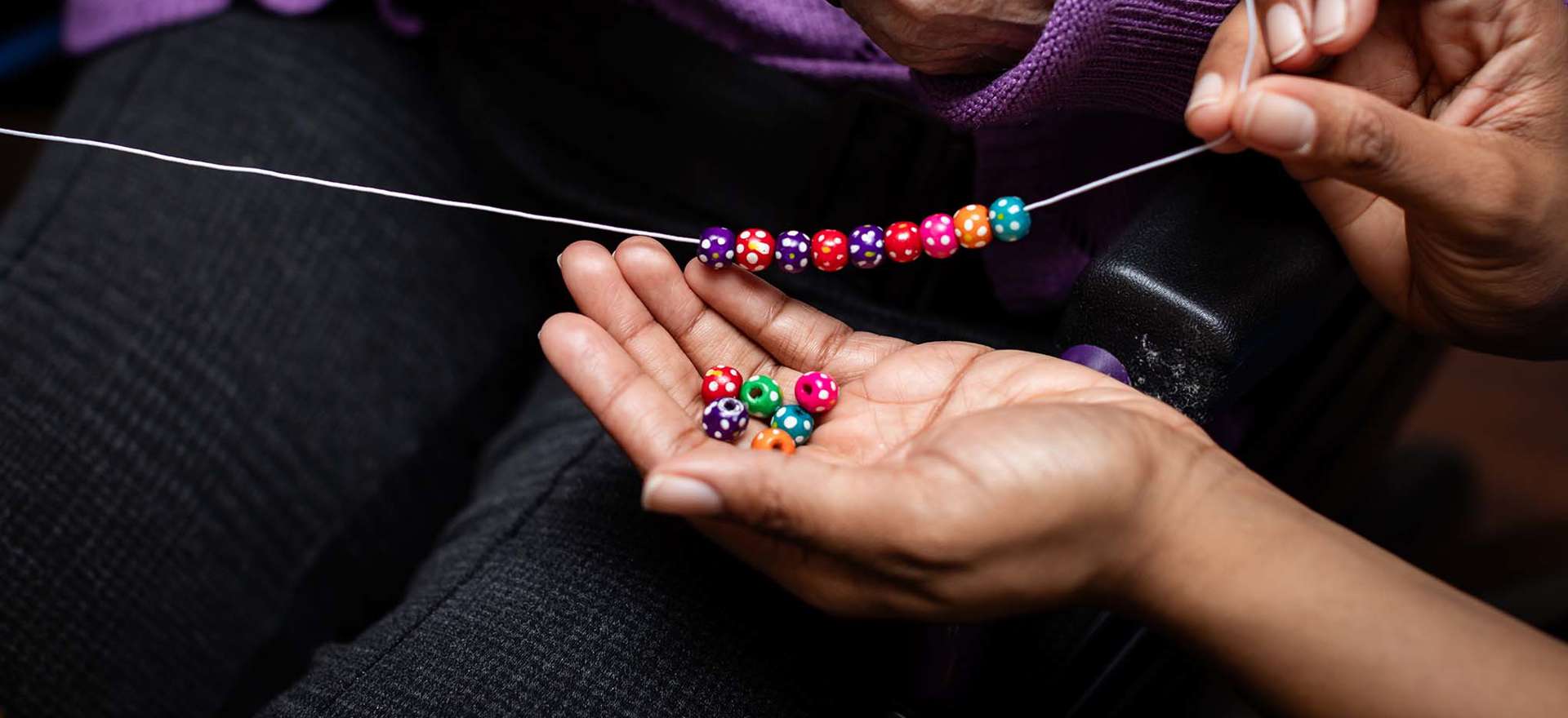A staff member supports a resident to make a vibrant bracelet as part of the homes activities calendar