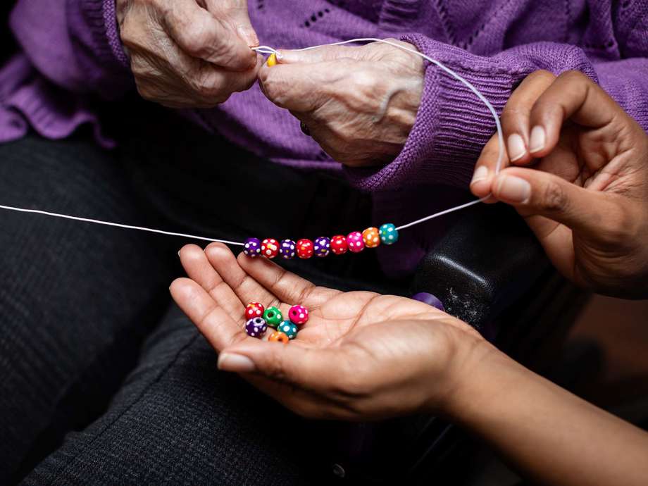 A staff member supports a resident to make a vibrant bracelet as part of the homes activities calendar