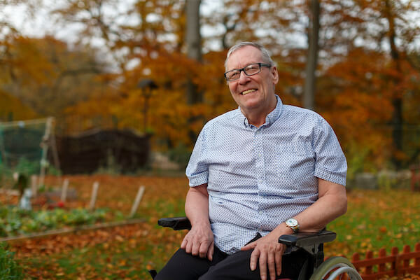 A care home resident smiles, he is enjoying time in the Autumnal garden 