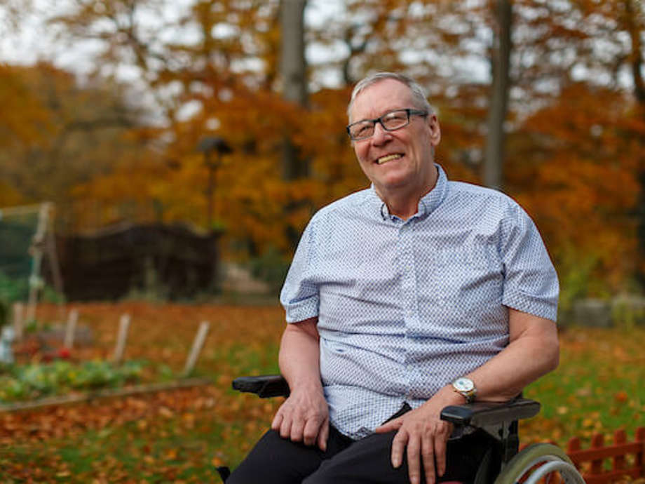 A care home resident smiles, he is enjoying time in the Autumnal garden