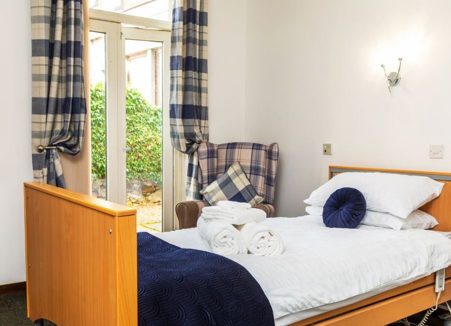 Care home bedroom in a modern white and navy color scheme. Wooden furniture complements the spacious feel created by large patio doors.