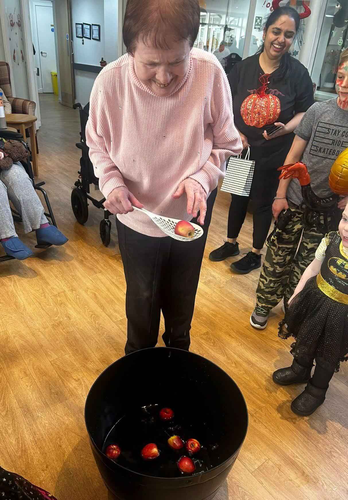 A care home resident enjoys a traditional Halloween game of 'dooking for apples'
