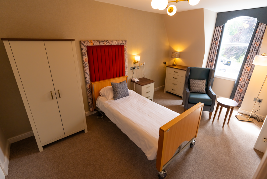 A modern, vibrant bedroom featuring orange and blue floral colours throughout. The room is spacious and features a wardrobe, bed, chair, bedside table, lamp and has gold accents throughout