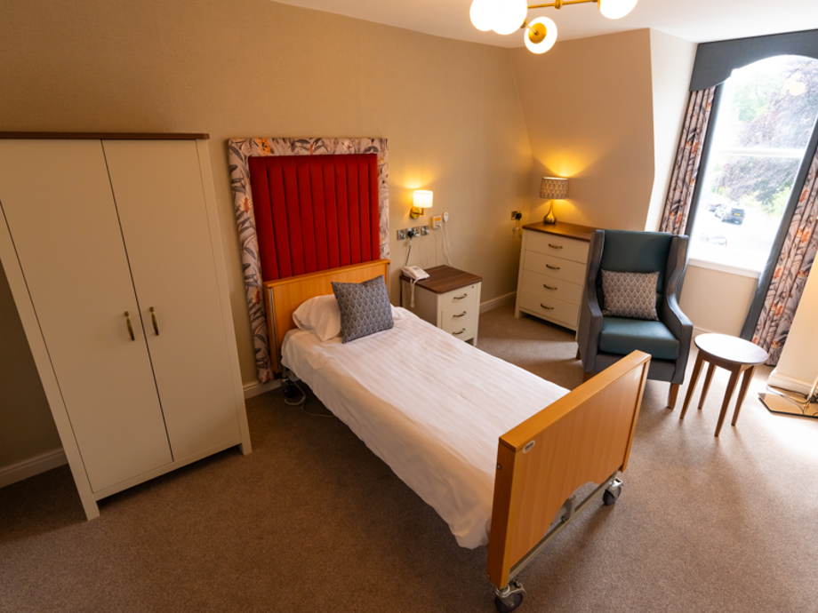 A modern, vibrant bedroom featuring orange and blue floral colours throughout. The room is spacious and features a wardrobe, bed, chair, bedside table, lamp and has gold accents throughout