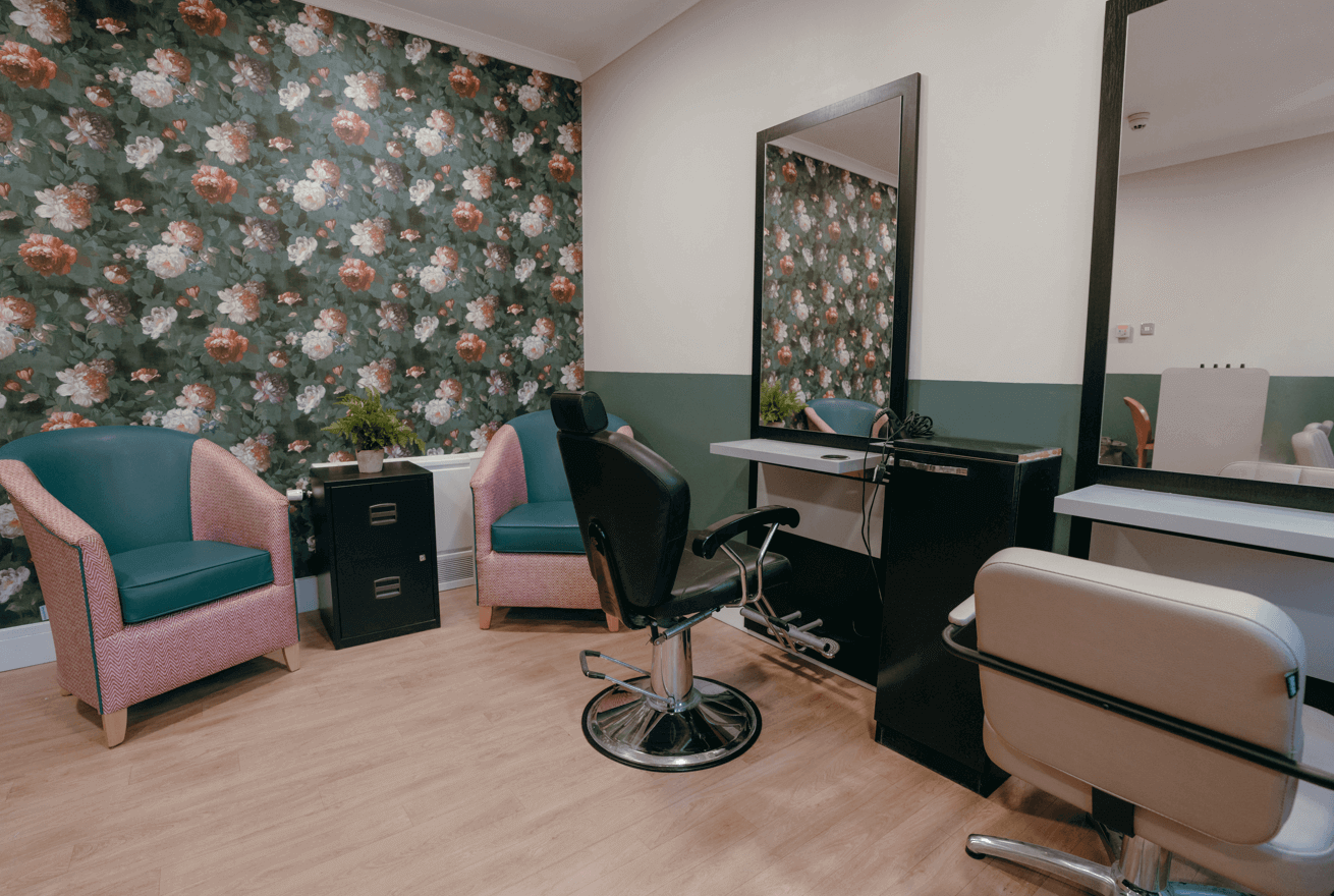 A pink and green salon space with a bold feature wall, two matching armchairs, and hairdressing stations.  