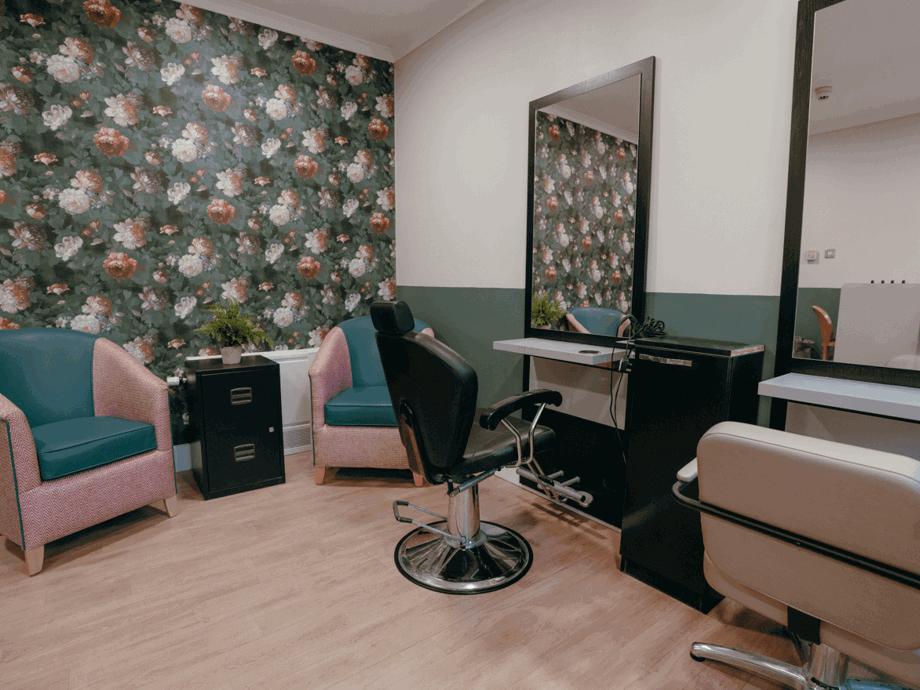 A pink and green salon space with a bold feature wall, two matching armchairs, and hairdressing stations.  