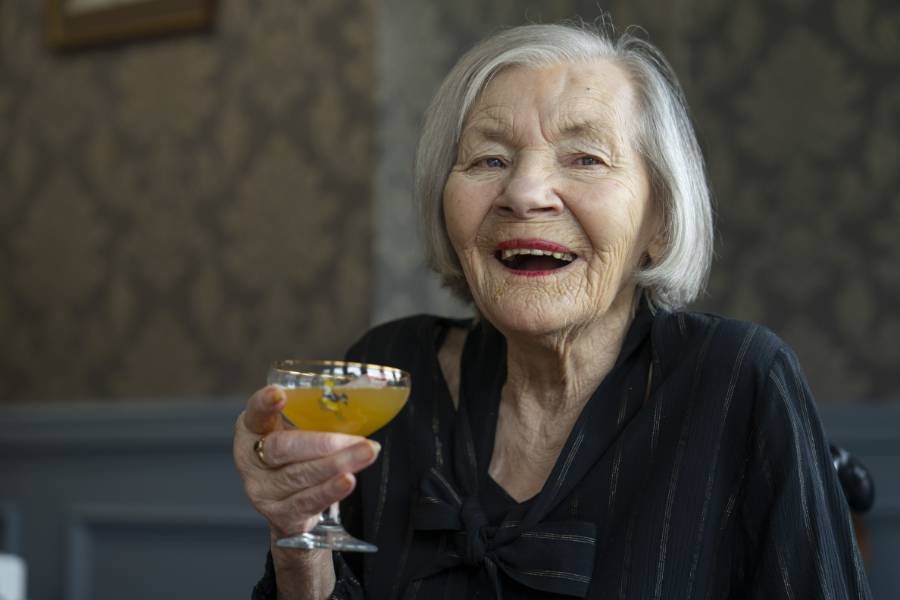 A care home resident smiles brightly, holding up a colourful cocktail 