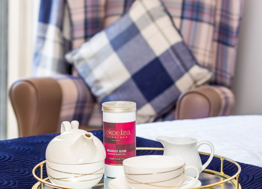 Cosy teatime treat. Tea set with Pukka tea on a tray rests on a bed. A navy tartan chair adds a touch of comfort