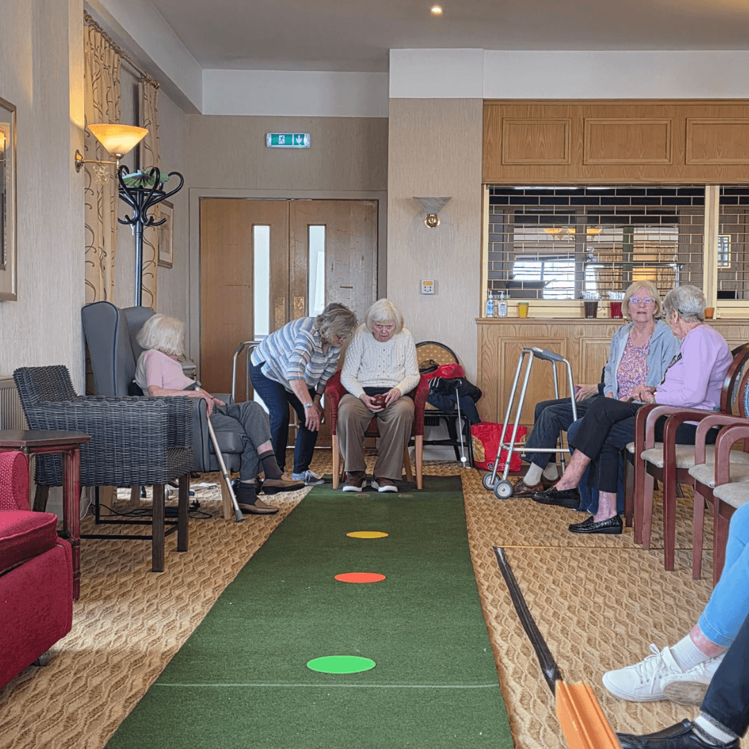 A faux grass bowls court has been set up to the length of the room - a resident i preparing to roll their ball as the spectators line the grassy court