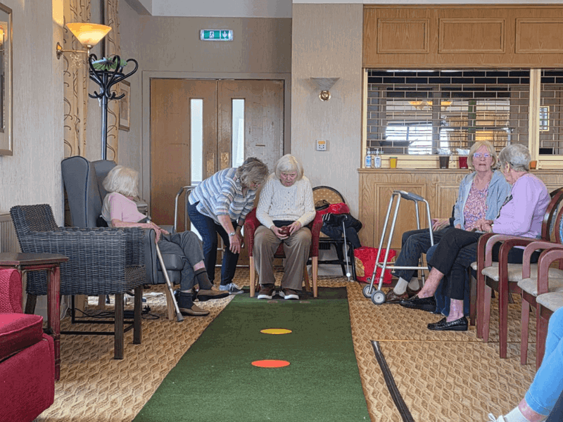A faux grass bowls court has been set up to the length of the room - a resident i preparing to roll their ball as the spectators line the grassy court