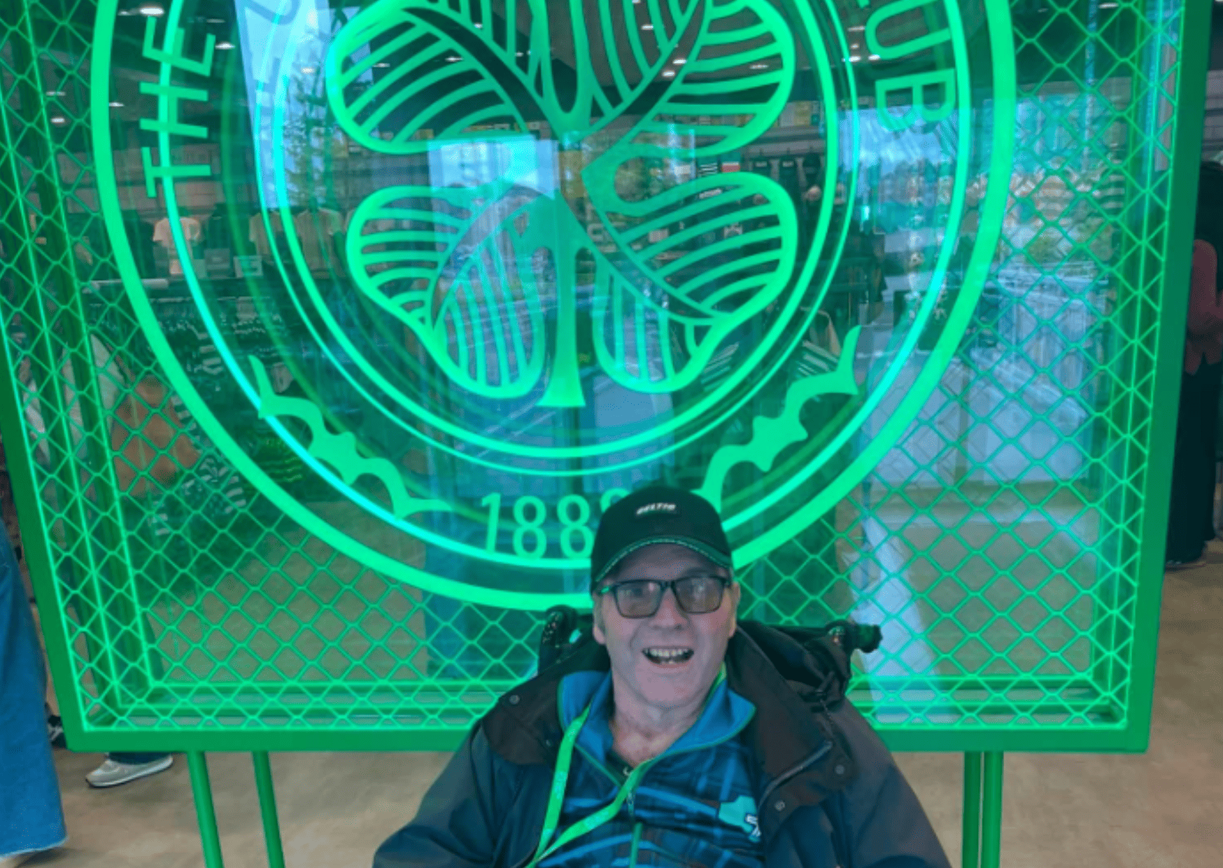 A resident poses in front of a large green sign featuring the Celtic Football Club logo 