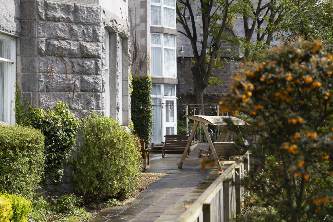 Serene care home garden featuring a relaxing patio with comfortable seating. Lush greenery surrounds the space, creating a tranquil atmosphere.