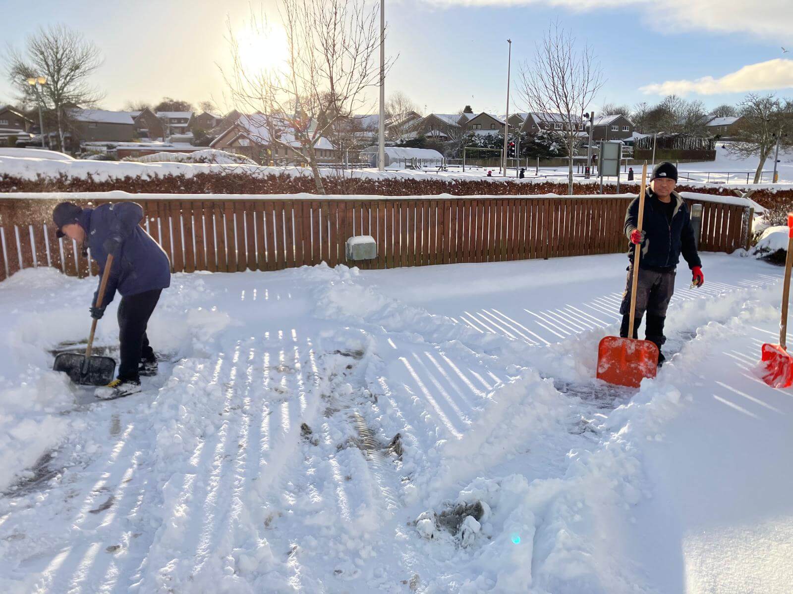 two staff members with snow shovels are busy at work, clearing the care homes car park 
