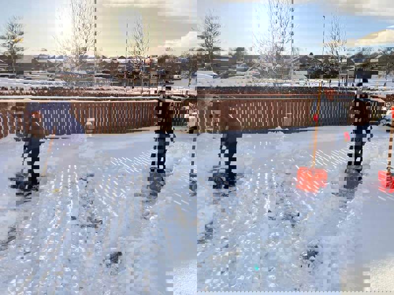 two staff members with snow shovels are busy at work, clearing the care homes car park 