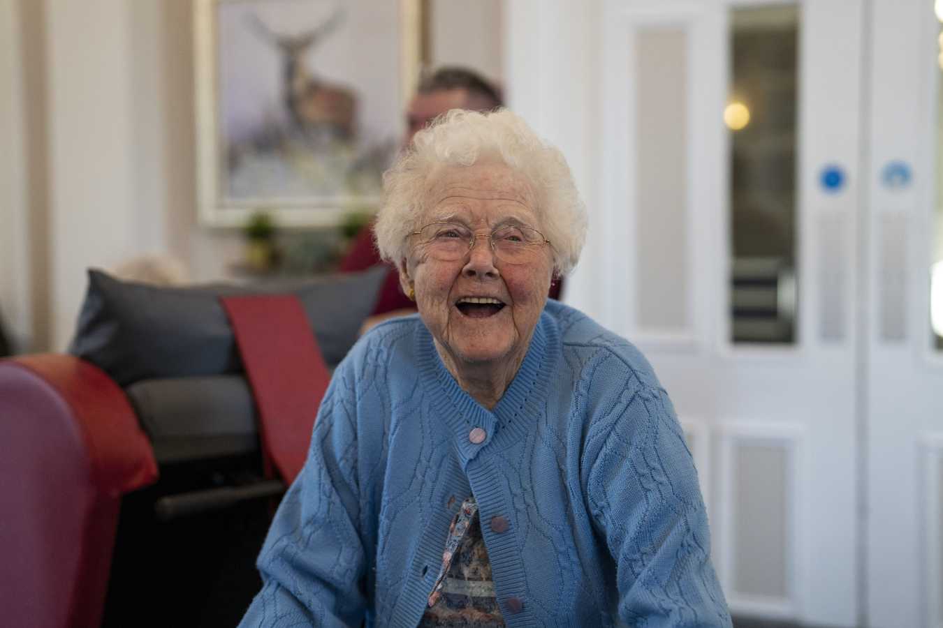 A woman in blue laughs while walking through a communal lounge