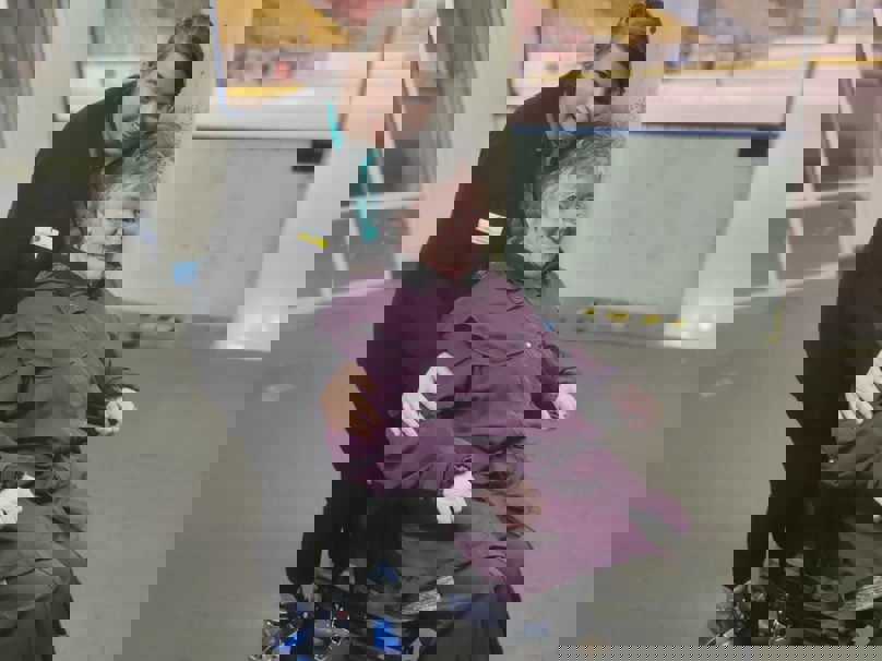 Staff member Ana stands behind resident Lynn, who is seated in a wheelchair eagerly awaiting her turn on the ice rink