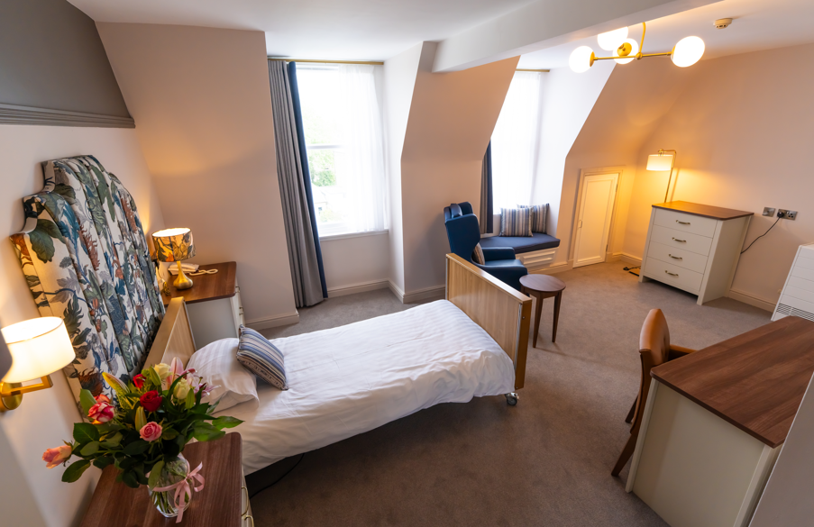 A spacious bedroom with an assortment of storage, seating, and cosy facilities. The room features colourful decor, with a modern and elegant appeal