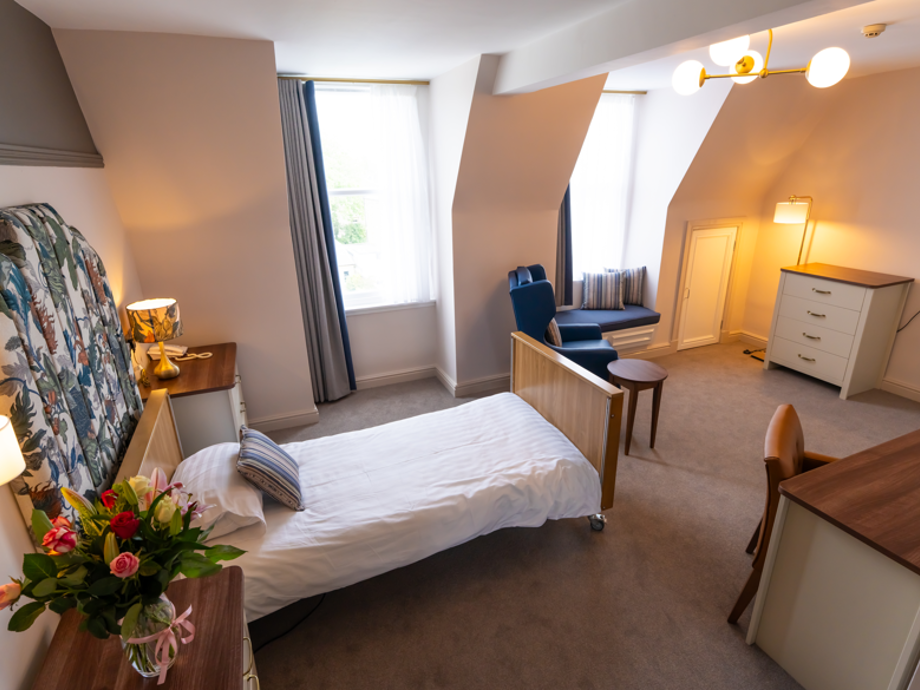 A spacious bedroom with an assortment of storage, seating, and cosy facilities. The room features colourful decor, with a modern and elegant appeal