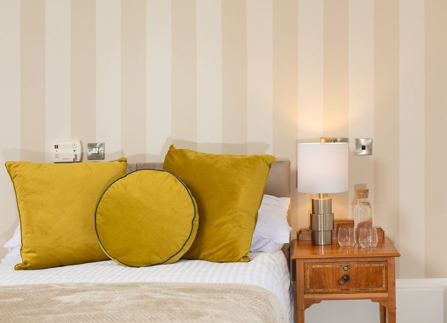 Inviting bedroom with comfy bed adorned with yellow cushions, a wooden nightstand with a lamp for reading, and a glass of water