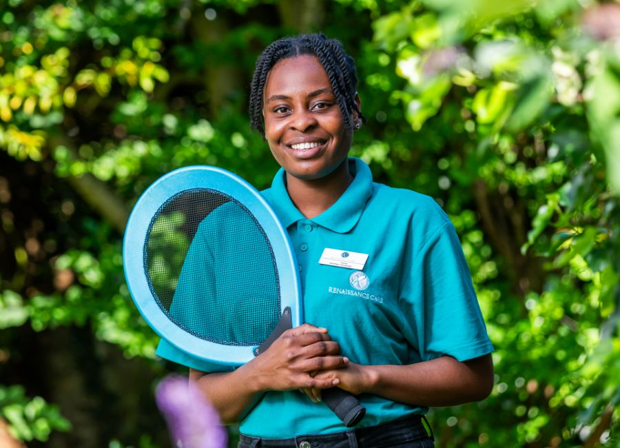 Care home staff member promotes an active lifestyle, holding a tennis racket while in uniform. 