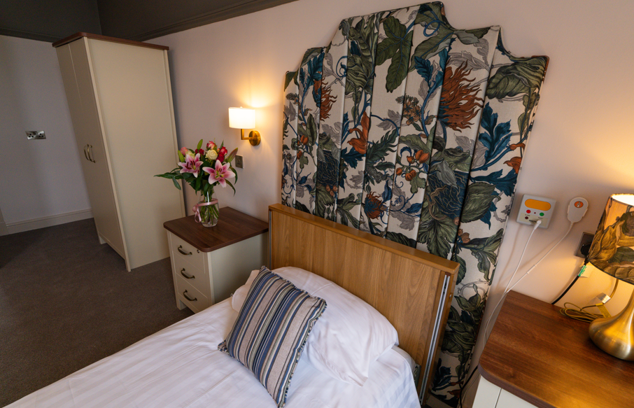 Newly renovated bedroom with a colourful floral headboard as the focal point. The room is cosy, with accent lighting and flowers