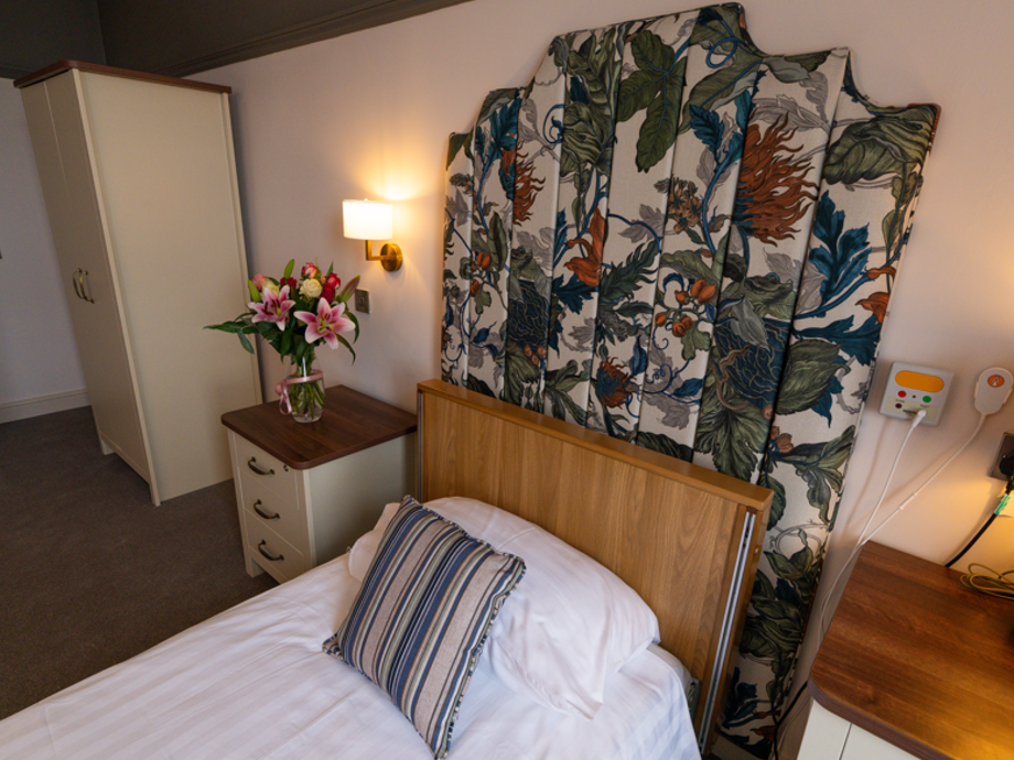 Newly renovated bedroom with a colourful floral headboard as the focal point. The room is cosy, with accent lighting and flowers