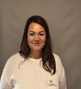 A headshot of manager Jemma Critchley. She is wearing a cream jumper, and has shoulder-length dark hair. 