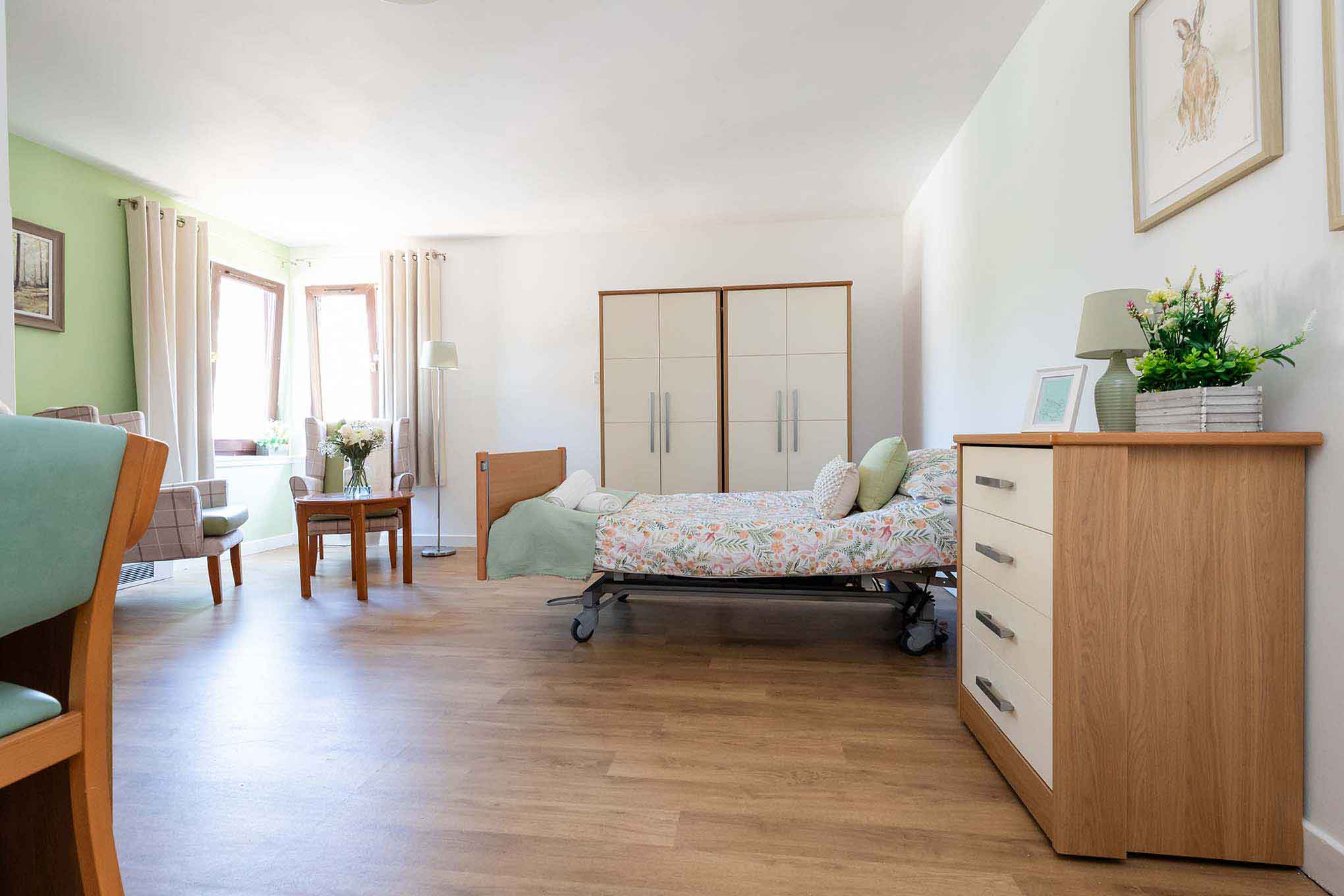 A large bedroom offering ample space for socialising with family and friends. large windows overlook the homes ground, with a dining table and chairs, bed, wardrobe and home comforts. 
