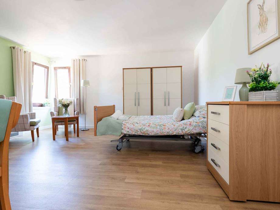 A large bedroom offering ample space for socialising with family and friends. large windows overlook the homes ground, with a dining table and chairs, bed, wardrobe and home comforts.