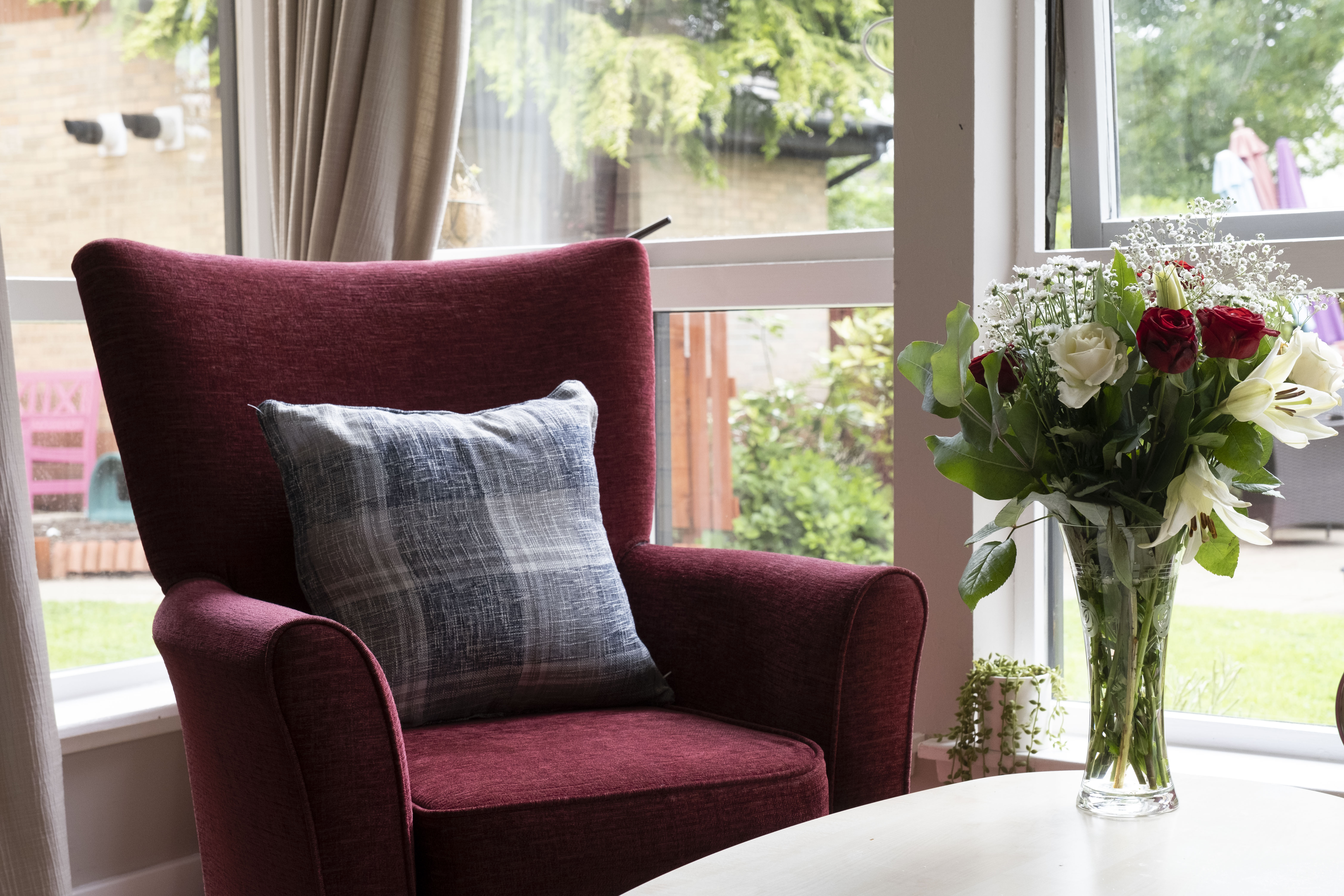 a decorative shot of a red armchair next to the window looking out at the garden, and a white wooden table with fresh roses 