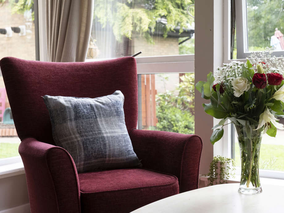 a decorative shot of a red armchair next to the window looking out at the garden, and a white wooden table with fresh roses