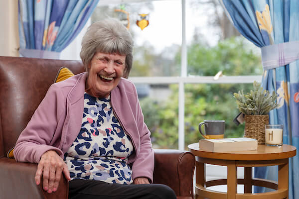 A woman sitting on an armchair in a communal lounge is belly laughing