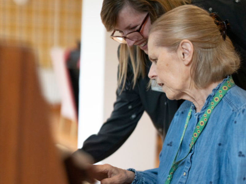 A staff member supports a care home resident to play piano