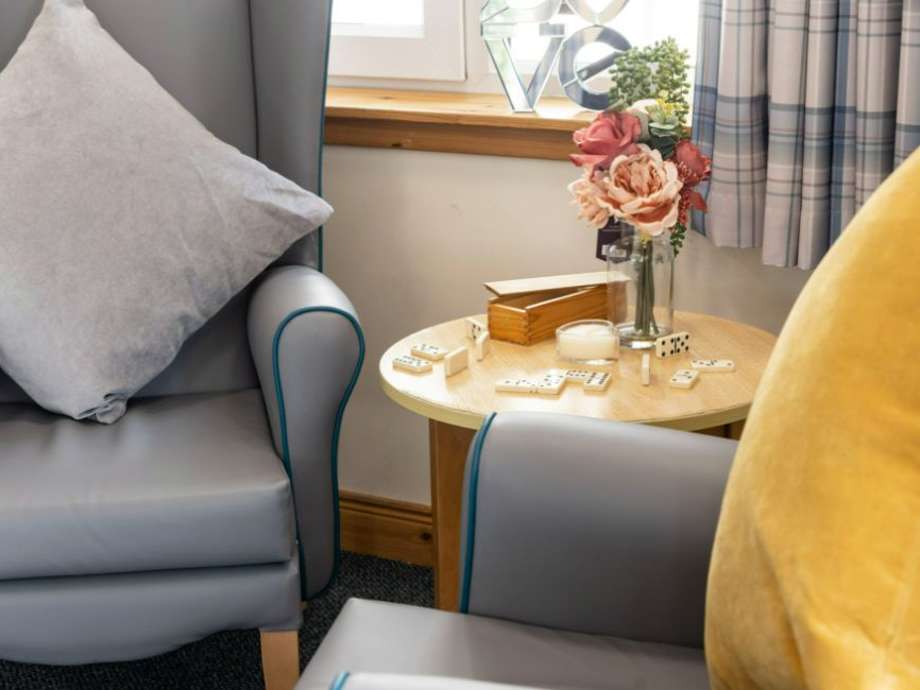 A communal lounge shows two armchairs and a side table set up for a game of dominoes