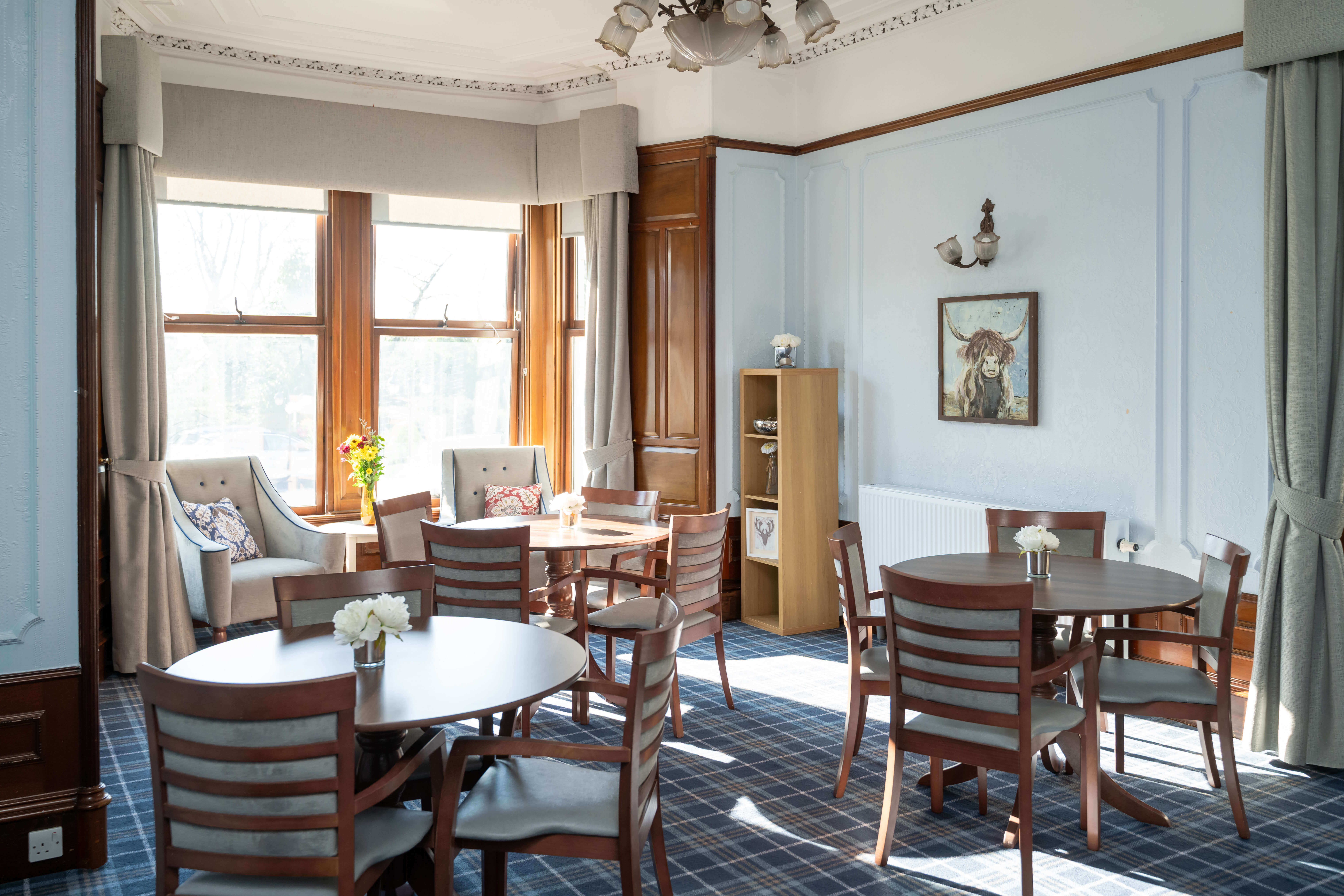 This wide shot captures the lounge area with its arrangement of tables and chairs, emphasising the tall ceilings, detailed cornicing, and prevalent Scottish themes.