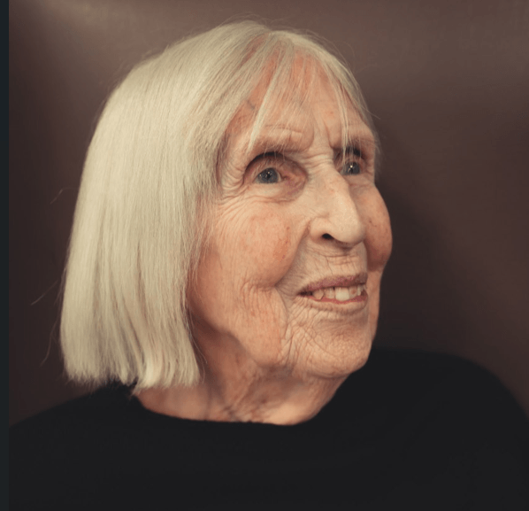 A profile portrait of an elderly woman with straight, chin-length white hair. She is looking off-camera with a gentle smile.